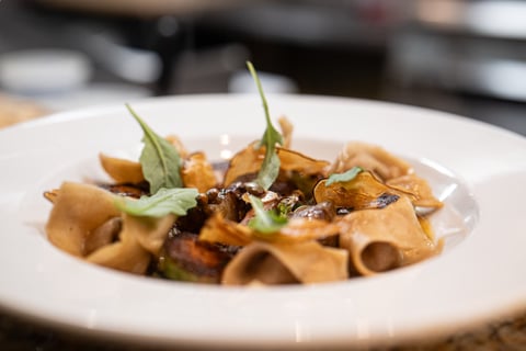 Wide house pappardelle with braised meat, capers and arugula in a white bowl