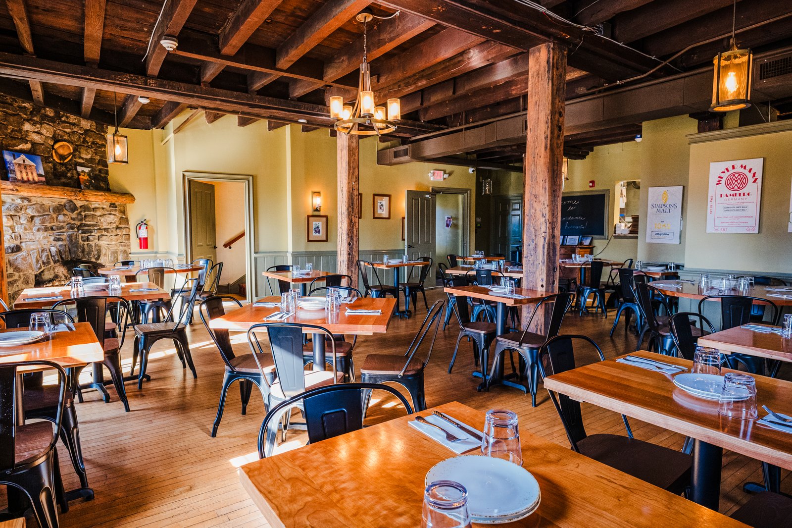 The dining room at Concordance Ferments set for service beneath exposed beams and a stone hearth