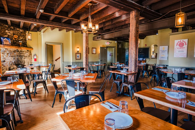 The dining room at Concordance Ferments set for service beneath exposed beams and a stone hearth