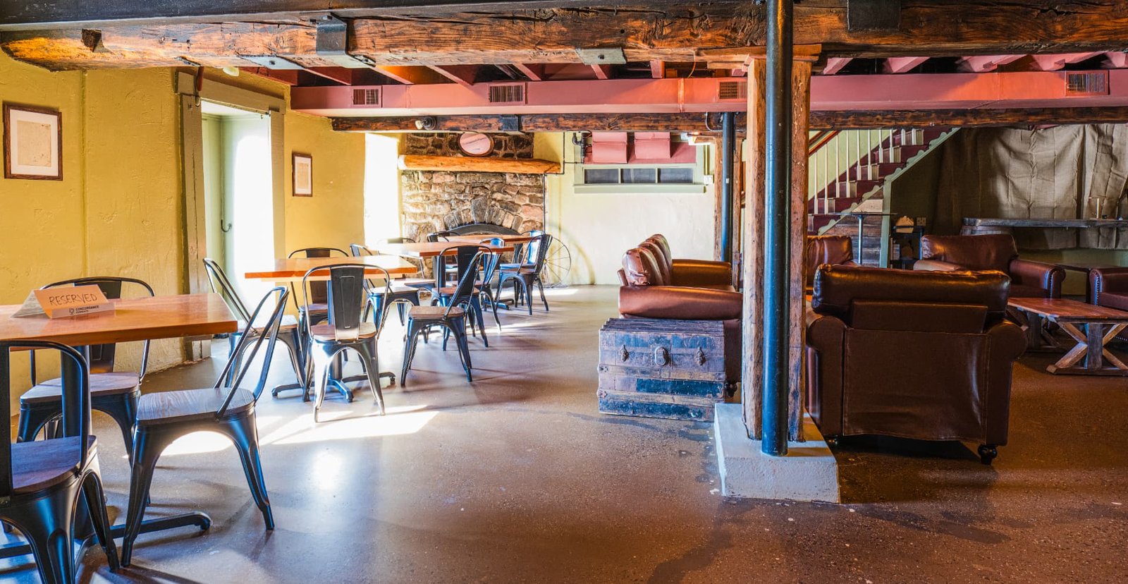 The downstairs lounge at Concordance Ferments — café tables, leather armchairs and a stone fireplace